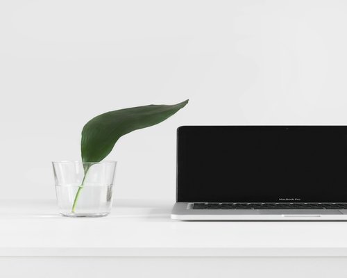 A workspace desk setup containing a modern laptop computer, notebook, and a clean glass of water