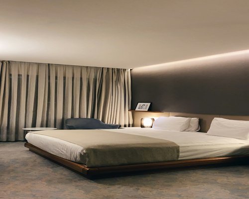 A dark cozy bedroom interior with a neatly arranged bed and soft ambient light
